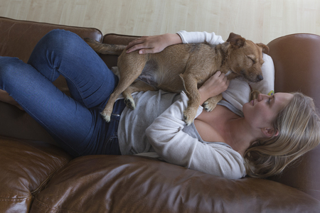 Ariel view of a woman cuddling her pet dog on a leather sofa.の写真素材