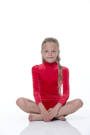 A young girl sitting on the floor crossed legged dressed in a leotard with a white background. She is looking at the camera and smiling.の写真素材