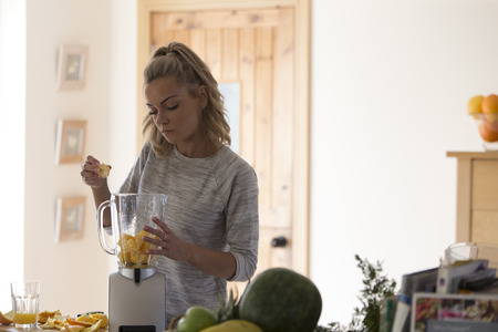 Young woman putting orangs in a blender to make a smoothie.の写真素材