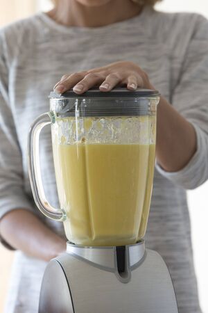 Close up view of a womans hands on a blender, mixing up a fruit smoothie.の写真素材