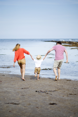 Young two parent family at the beach with their young son. They are all holding hands and swinging the little boy.の写真素材