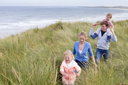 A young family of four walking through long grass next to the beach. They are wearing casual clothing and are smiling.の写真素材