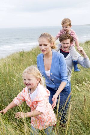 Close up of a young family of four walking through long grass next to the beach. They are wearing casual clothing and are smiling.の写真素材