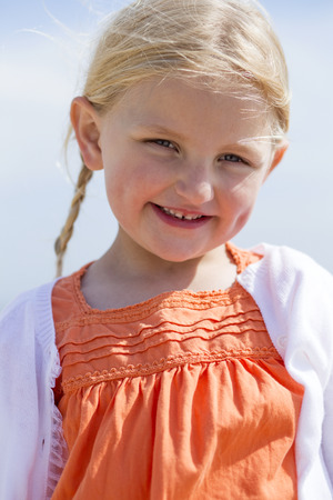 Close up of a beautiful little girl outdoors. She is wearing casual clothing and smiling at the camera.の写真素材