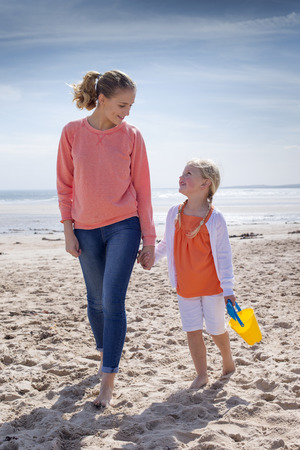 Young mother and daughter walking along with beach. They are looking at each other and smiling.の写真素材