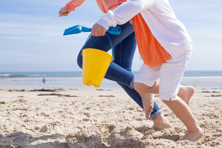 Mother and Daughter running along the beach. Only their legs can be seen, the little girl is holding a bucket and spade.の写真素材