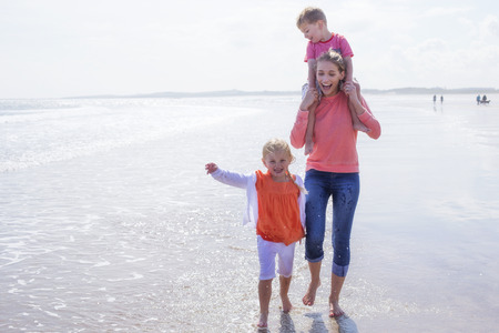Young single mother at the beach with her son and daughter. They are laughing and are barefoot in the water.の写真素材