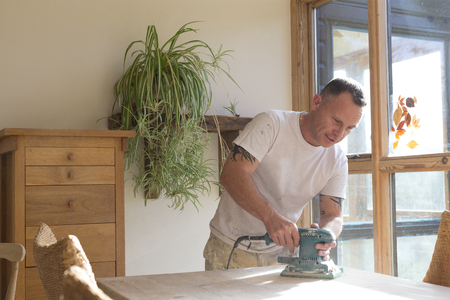 Wood joiner using an electric sander to smoothen a table surfaceの写真素材