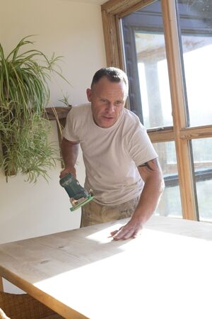 Wood joiner using an electric sander to smoothen a table surfaceの写真素材