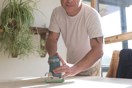 Wood joiner using an electric sander to smoothen a table surfaceの写真素材