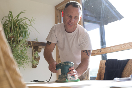 Wood joiner using an electric sander to smoothen a table surfaceの写真素材