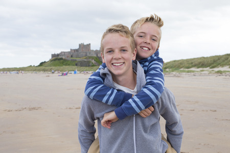 Teenage brothers at the beach with a castle in the background. They are wearing casual clothing and smiling at the camera.の写真素材