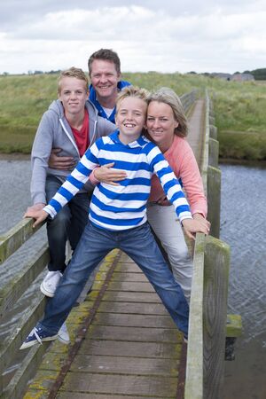 Family of four standing on a bridge and smiling at the camera. They are wearing casual clothing and look very happy and content.の写真素材