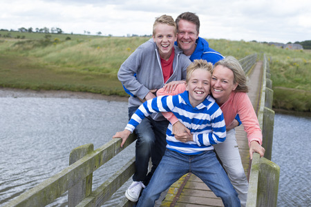 Family of four on a bridge over water. They are wearing casual clothing and smiling at the camera.の写真素材