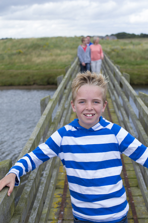 Portrait of a young boy on a bridge with his family in the background. He is smiling at the camera and wearing casual clothing.の写真素材
