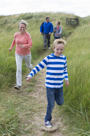 Family of four running down the sand dunes at the beach. They are wearing casual clothing and smiling.の写真素材