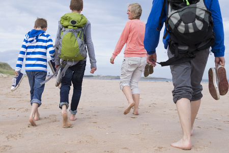 Family of four walking along the beach barefoot. They are wearing warm casual clothing.の写真素材