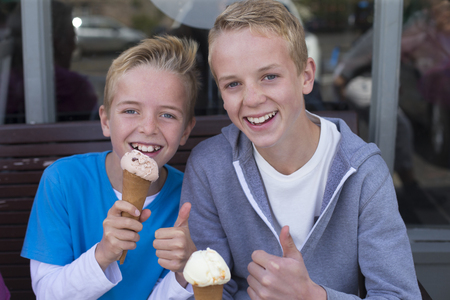 Brothers enjoying ice cream outside of a shop. They are wearing casual clothing and smiling at the camera.の写真素材