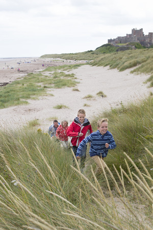Family of four running up the sand dunes at the beach. They are wearing warm casual clothing and a castle can be seen in the background.の写真素材