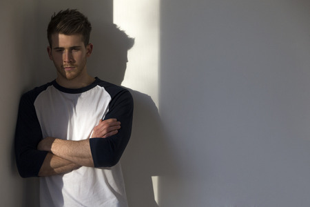 Portrait of an attractive young man, standing against a white wall with sunlight from the window shining on him.の写真素材