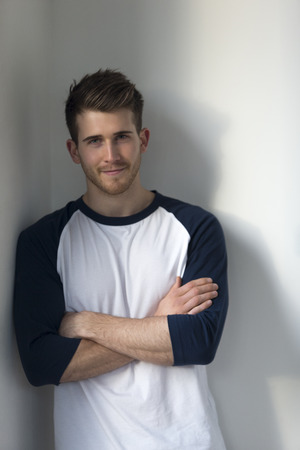 Portrait of an attractive young man, standing against a white wall and smiling for the camera with his arms crossed.の写真素材