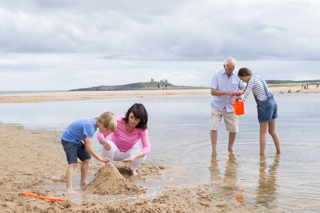 Grandparents and grandchildren are playing together on the beach. They all look happy playing with the sand and water.の写真素材