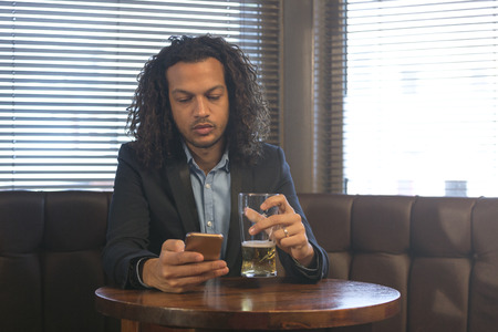 Young man using his smartphone whilst enjoying a beer in a bar.の写真素材