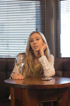 Young woman sitting on her own in a bar with a glass of wine and a smartphone.の写真素材