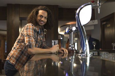 Young man standing at a bar with a pint, smiling for the camera.の写真素材