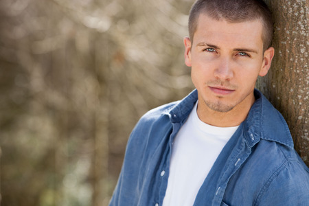 Close up shot of an attractive young man leaning against a tree outdoorsの写真素材