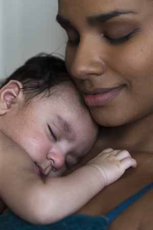 Clsoe up shot of a young mother enjoying a cuddle with her baby son sleeping on her chest.の写真素材