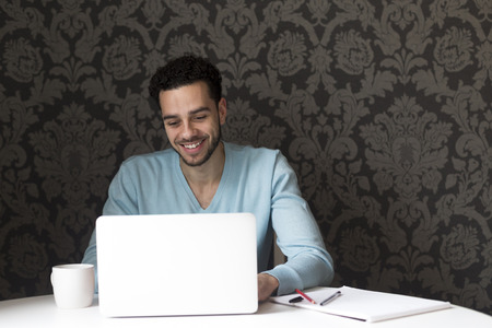 Young man using a laptop at home. He is looking at the screen and smiling.の写真素材