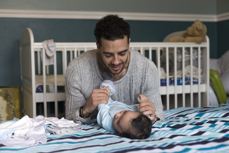 Young father is playing lovingly with his baby son, who is lying on his parents bed.の写真素材