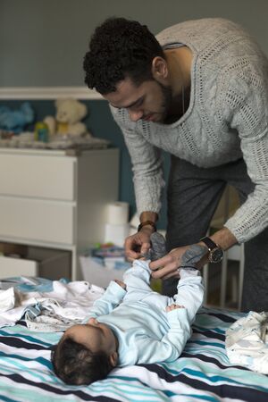 Young father is putting some socks on his baby son, who is lying on his parents bed.の写真素材