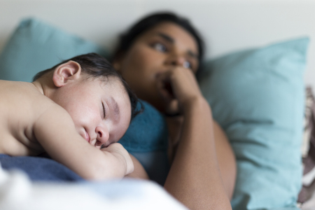 Baby asleep in bed on his mother's chest, who is enjoying the break from stressful parenting.の写真素材