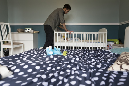 Young father checking on his baby son, who is asleep in a copt in the bedroom.の写真素材