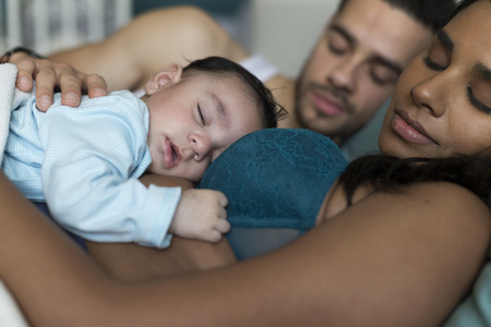 Young couple asleep in bed with their baby son sleeping on his mothers chest.の写真素材