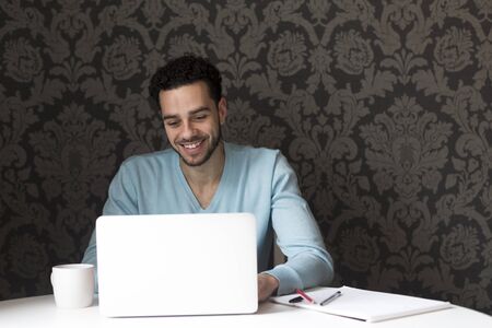 Young man using a laptop at home. He is looking at the screen and smiling.の写真素材