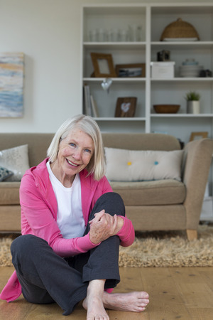 Senior woman sitting on the floor. She is smiling and looking at the camera.の写真素材
