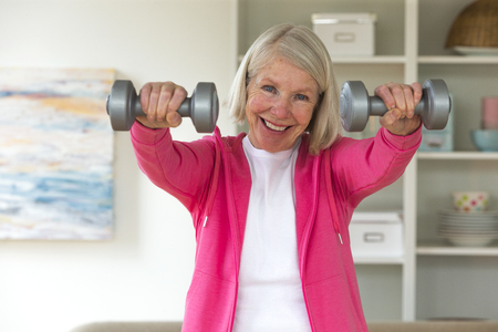 Senior lady smiling at the camera whilst using dumbbells.の写真素材