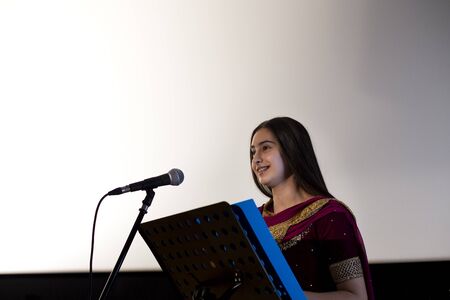 Female student making a speech. She is standing at a podium and smiling to the crowd.の写真素材
