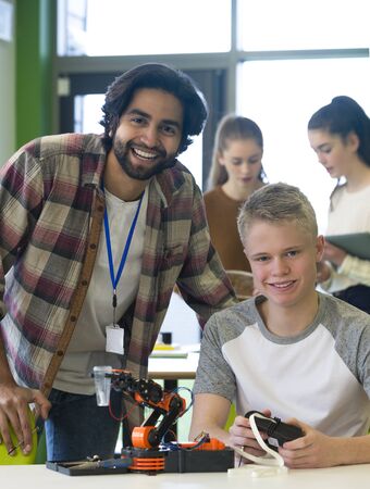 Student and teacher smiling at the camera in class. They are working on a robotic arm together.