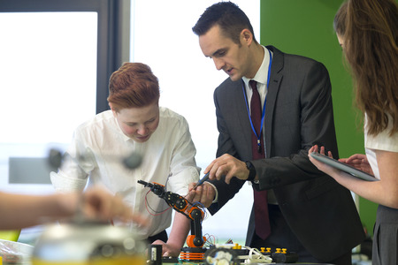 Two students are building a robotic arm in school. The teacher is helping them and they are...