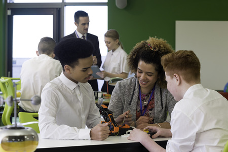 Students in school are building a robotic arm. The teacher is discussing their technique with them.