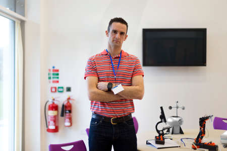 Male teacher standing in a science and technology classroom. He has his arms folded and is looking at the camera.の写真素材
