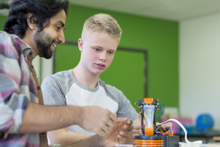 Teacher and student building a robotic arm and discussing the technology in a classroom.