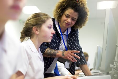 Female teacher with tattoos helping one of her students, who is doing work on a computer.