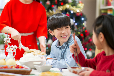 Chinese boy enjoying his Christmas dinner with his family. He is sharing a giggle with his sister.の写真素材