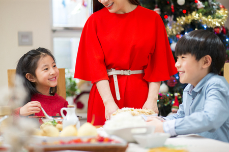 Chinese family having Christmas Dinner. The mother is standing up, dishing food to everyone. The children are laughing together.の写真素材