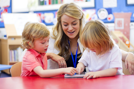 Female nursery teacher using a digital tablet with two students in the classroom.の写真素材